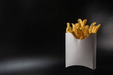 Kartondan yapılmış beyaz kağıt ambalajı. Kızarmış patates kızartması, konteynırda. Fast food, üretim konsepti. Siyah arka plan. Metin eklemek için bir yer. Boşluğu kopyala.