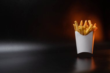 Kartondan yapılmış beyaz kağıt ambalajı. Kızarmış patates kızartması, konteynırda. Fast food, üretim konsepti. Siyah arka plan. Metin eklemek için bir yer. Boşluğu kopyala.