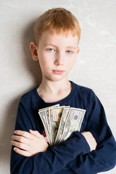 Рыжеволосый мальчик, прислонившись к груди, держит первые заработанные деньги, доллары. Взгляд уверенного в себе человека — стоковое фото
