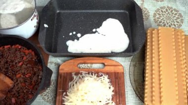 Masanın üzerinde İtalyan lazanyası pişirmek için gerekli tüm malzemeler var. Pişirilmiş beşamel sosu, pişirme çarşafının altına sürülür..