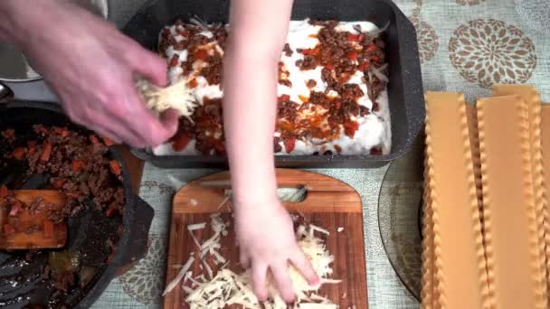 Na stole są wszystkie składniki do gotowania włoskiej lazanii. druga warstwa sera parmezanu jest posypana świeżo przygotowanym sosem bolońskim z mięsem, warzywami i przyprawami — Wideo stockowe