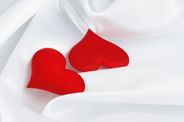 Dvě červené srdce na bílého hedvábí — Stock fotografie