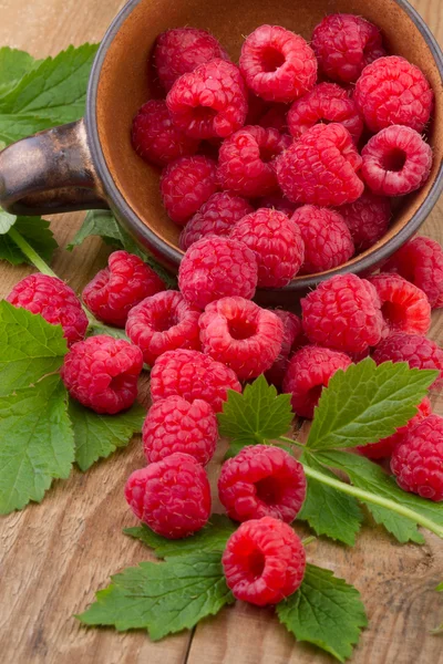 Verse frambozen met bladeren in een kom op houten tafel — Stockfoto