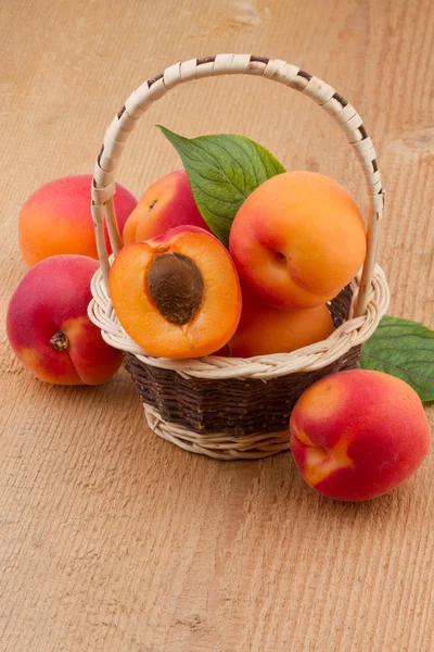 Ripe apricots in wicker basket on wooden background — Stock Photo, Image