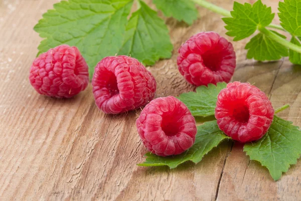 Raspberries with leaves over wooden background — Stock Photo, Image