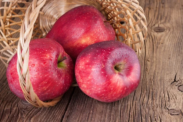 Rote Äpfel im Korb auf hölzernem Hintergrund — Stockfoto