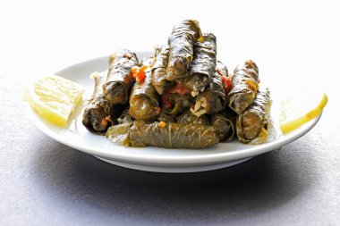 Dolma, pirinç ile doldurulmuş üzüm yaprakları ve beyaz bir tabakta et, ön manzara.