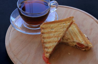 Çedar peynirli tost ve siyah arkaplanda Türk sosisi çayı.