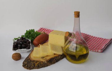 Various types of cheese on a wooden board. Olive oil, crackers, sausage, parsley, walnuts and olives in glass bottle on white background.
