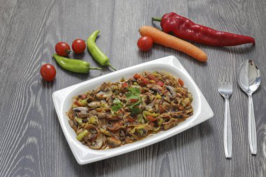 Biber ve domates, soğan, sarımsak ve zeytinyağıyla sotelenmiş mantar, beyaz bir tabakta, ahşap arka planda..