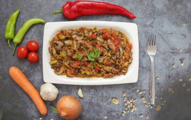 Biber ve domates, soğan, sarımsak ve zeytinyağıyla sotelenmiş mantar, beyaz bir tabakta, ahşap arka planda..