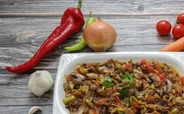 Biber ve domates, soğan, sarımsak ve zeytinyağıyla sotelenmiş mantar, beyaz bir tabakta, ahşap arka planda..