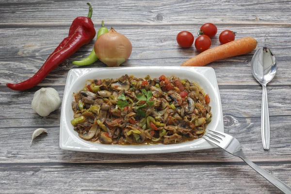 Biber ve domates, soğan, sarımsak ve zeytinyağıyla sotelenmiş mantar, beyaz bir tabakta, ahşap arka planda..