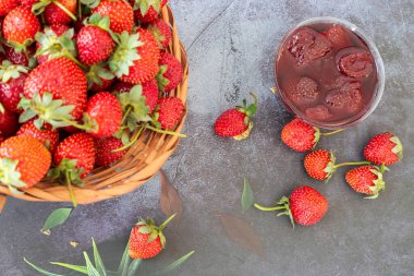 Sepette çilek ve ev yapımı çilek reçeli bir kasede, ahşap bir masada.