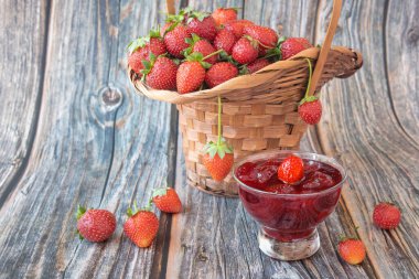 Sepette çilek ve ev yapımı çilek reçeli bir kasede, ahşap bir masada.