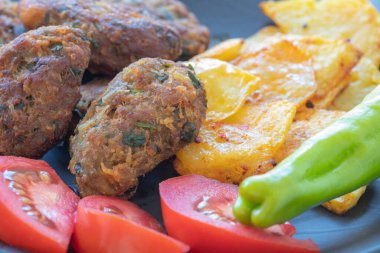 Cyprus meatballs, tomatoes, french fries, peppers. Beautiful presentation on a black plate.