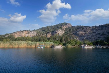 The rock-cut temple tombs of the ancient city of Kaunos in Dalyan, Mula, Turkey. Beautiful view of Dalyan river with reed beds, excursion boats and carved tombs in the background.