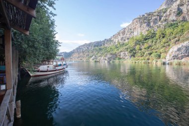 The rock-cut temple tombs of the ancient city of Kaunos in Dalyan, Mula, Turkey. Beautiful view of Dalyan river with reed beds, excursion boats and carved tombs in the background.