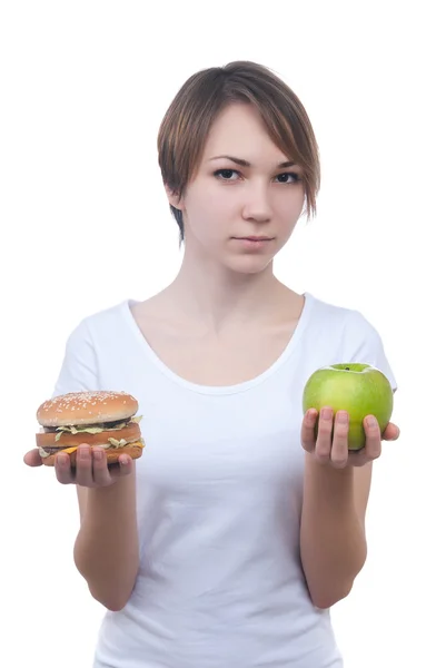 Девушка делает выбор между яблоком и гамбургером Лицензионные Стоковые Фото