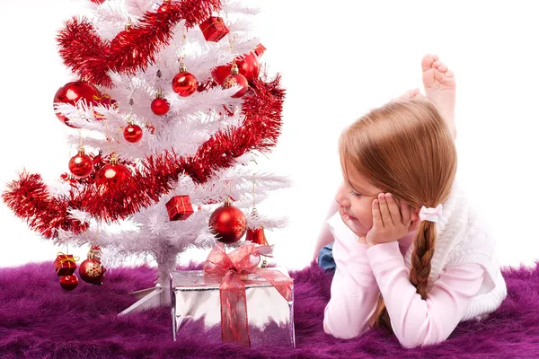 Mädchen liegt auf dem Teppich neben einem weißen künstlichen Weihnachtsbaum mit Geschenken — Stockfoto