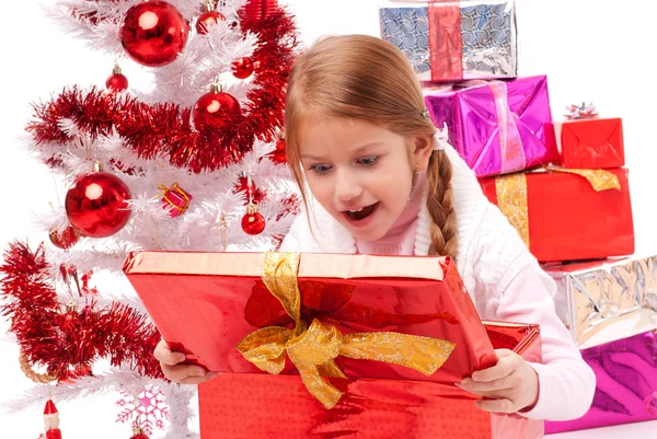 Girl opening Christmas gift near the white artificial Christmas trees Royalty Free Stock Photos