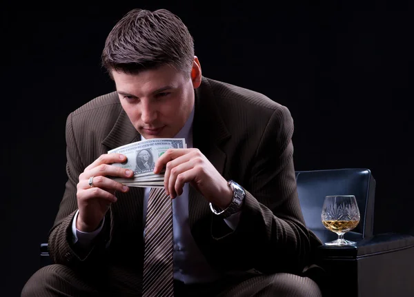 Young businessman with money and an alcoholic beverage sitting in the chair — Stock Photo, Image