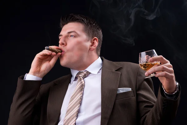 Jeune homme d'affaires assis sur un canapé avec une boisson alcoolisée et un cigare — Photo