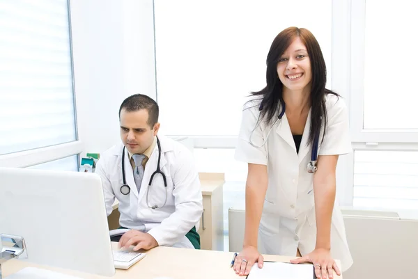 Happy nurse behind the doctor is working on a laptop — Stock Photo, Image