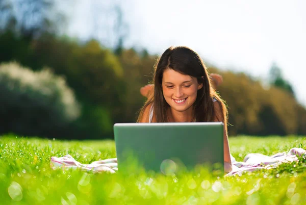 Retrato de uma jovem mulher bonito com um laptop deitado na grama — Fotografia de Stock