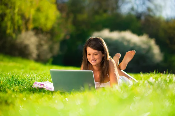 Retrato de uma jovem mulher bonito com um laptop deitado na grama - Ao ar livre — Fotografia de Stock