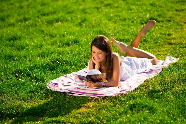 Une jeune femme allongée sur l'herbe et lisant un livre — Photo