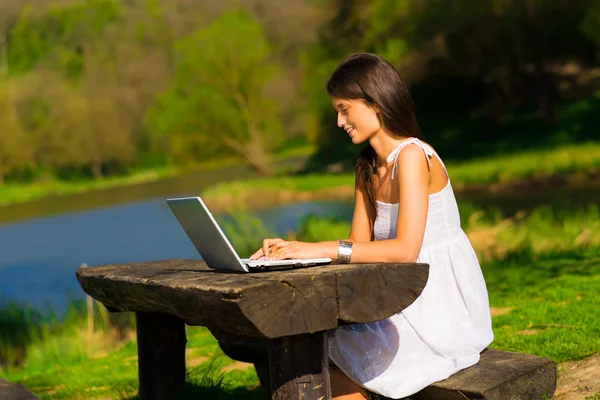 Giovane femmina con un computer portatile seduto un bellissimo lago — Foto Stock