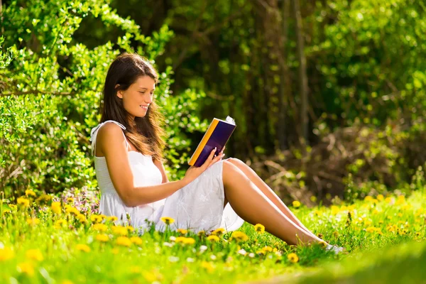 Une jeune femme allongée sur l'herbe et lisant un livre — Photo