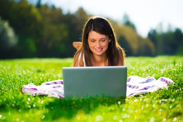 Portrait of a cute young female with a laptop lying on grass Stock Photo