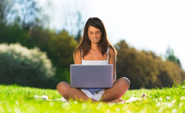 Schöne junge Frau sitzt im Park mit einem tragbaren Laptop lizenzfreie Stockbilder