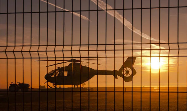 Helicopter at sunset behind fence — Stock Photo, Image