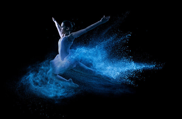 Young beautiful dancer jumping into blue powder cloud