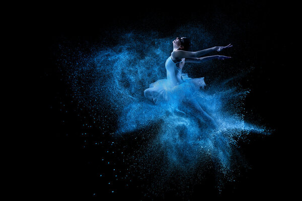 Young beautiful dancer jumping into blue powder cloud