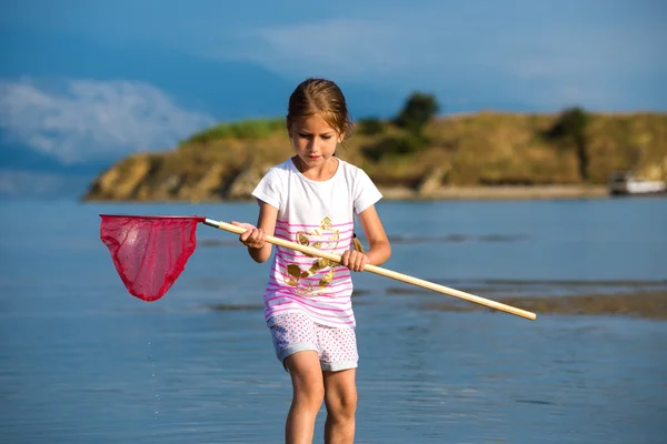 Beautiful little girl on the beach fishes — Stock Photo, Image