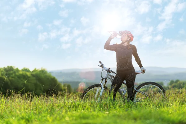 Deporte bicicleta mujer bebiendo en un prado — Foto de Stock