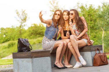 üç güzel kız selfie fotoğraf bir bankta olun.