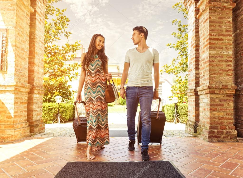 Young couple standing at hotel corridor upon arrival, looking for room, holding suitcases