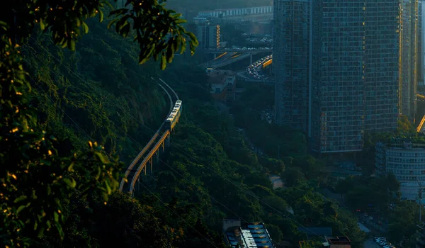 Chongqing, Çin 'deki Goose Ridge Parkı' nın yamaçlarındaki ağaçların arasından geçen tren yolu. Gün batımı üstüne dökülüyor.