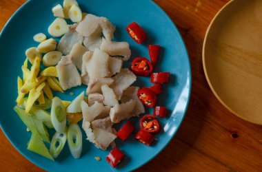 In the blue plate, there is hot water blanched pork, sliced garlic and green onion, and julienned ginger; in red are red chili peppers cut into small pieces, which look very spicy.