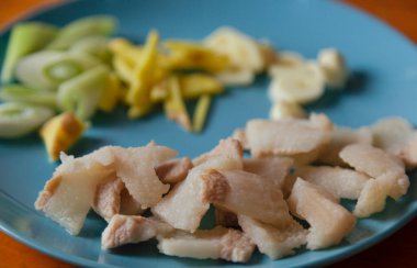 On the blue plate, there is hot water blanched pork, sliced garlic and scallions, and shredded ginger. These are the ingredients to be prepared for stir-frying Chinese food