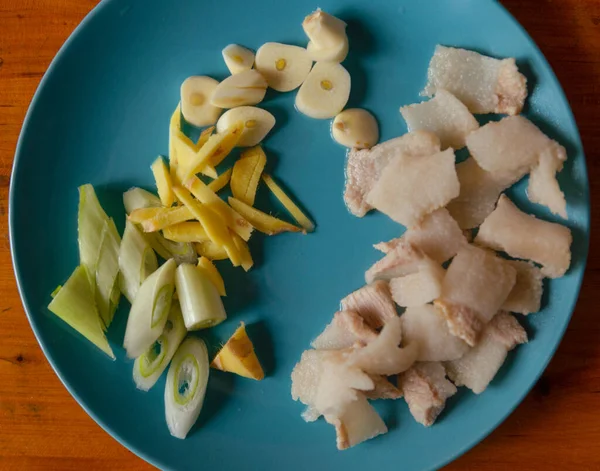 On the blue plate, there is hot water blanched pork, sliced garlic and scallions, and shredded ginger. These are the ingredients to be prepared for stir-frying Chinese food