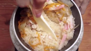Bir Shamoji pirinç küreğiyle karıştırılmış bir eli gösteren videoyu kapatın. Japon pilav tabağı Takikomi Gohan, sebze, kaka balığı ya da metal bir kasede bambu filizleri ile tatlandırılmış..