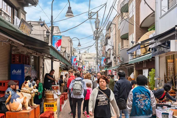 Tokyo, Japonya - 24 Ekim 2021: Yanaka-Ginza alışveriş caddesinde büyüyen pençeli Japon maneki-neko kedilerinin kapalı ve ağzı açık iki ahşap heykeli boyunca kalabalık geziniyor..