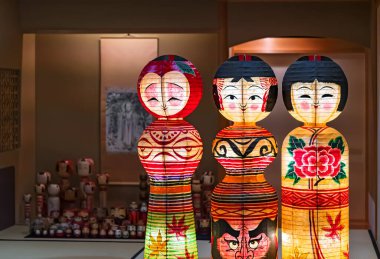 Tokyo, Japonya - 14 Ekim 2021: Japon geleneksel el yapımı Kokeshi bebeklerini gösteren ışıklı kağıt fenerler, Sugamo Koganji tapınağındaki momiji yaprakları, daruma yüzü veya kamelya ile süslenmiş..