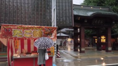 Tokyo, Japonya - 14 Ekim 2019: Yağmurlu bir günde Sugamo alışveriş sokağındaki Kgan-ji tapınağının önündeki Harajuku 'nun Harajuku adlı marketten takoyaki ahtapot topları alan yaşlı insanların videosu.